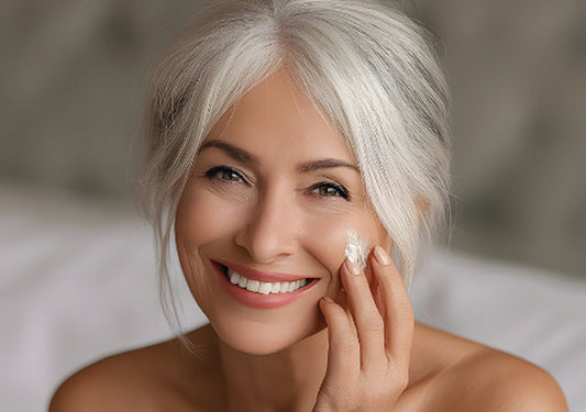 Smiling woman with silver white hair applying cream to her cheek