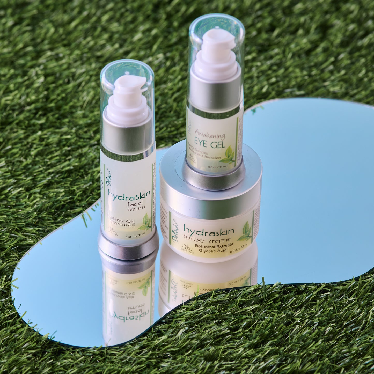 A pump bottle of Deluvia Awakening Eye Gel on a mirror with a Hydraskin Turbo Cream and Hydraskin Facial Serum