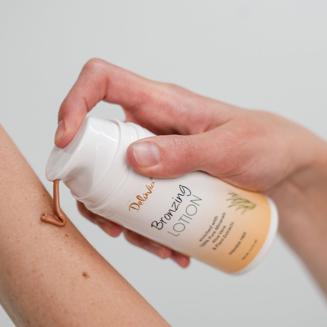 Hand applying Deluvia bronzing lotion to arm on a light background