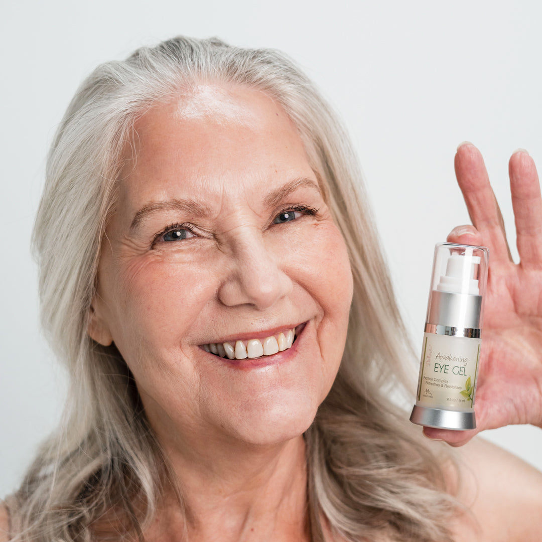 Smiling woman holding a bottle of eye gel with a plain background