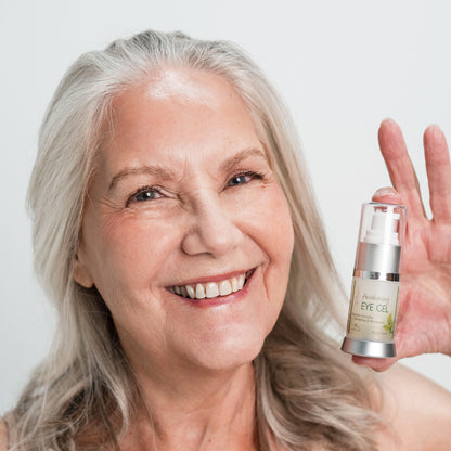 Smiling woman holding a bottle of eye gel with a plain background