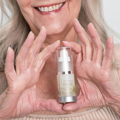 Woman smiling holding a bottle of Deluvia Awakening Eye Gel.