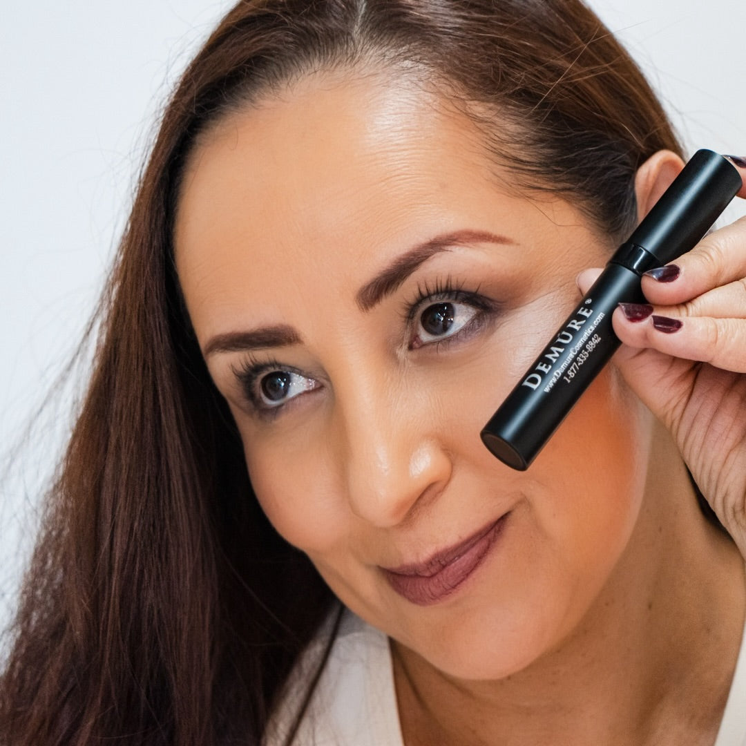 Woman holding Black Mascara tube close to her eye