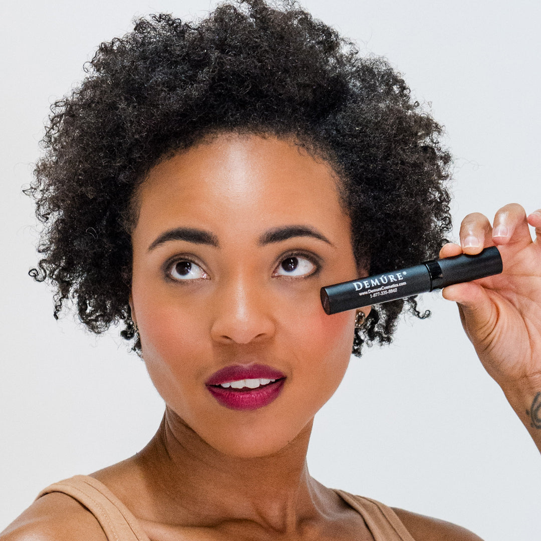 African American woman looking up holding Demure black mascara by her eye.