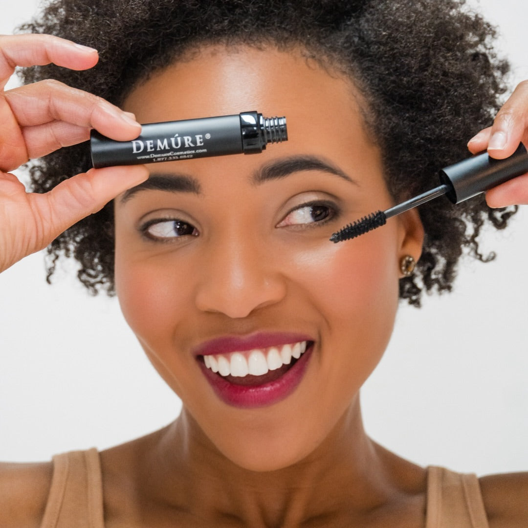 Woman applying mascara with a Demure mascara tube against a neutral background