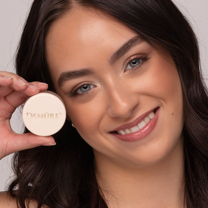 Smiling woman holding a jar of Blush Go Bronze near her cheek and wearing Go Bronze Blush