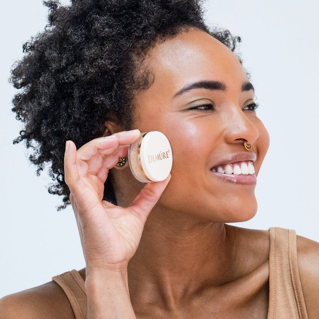 Woman wearing Demure Pink Fusion mineral blush and holding a jar against a neutral 