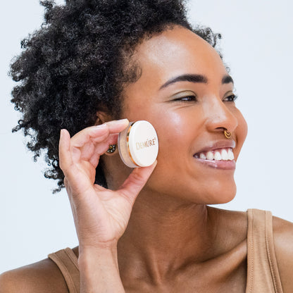 Woman wearing Demure Pink Fusion mineral blush and holding a jar against a neutral 