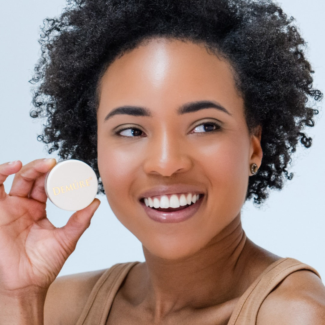 African American woman wearing Demure Bright Eye Concealer holding a jar near her eyes
