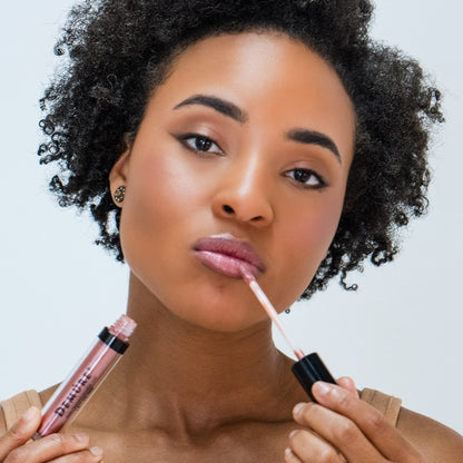 African American woman applying Demure Lip Gloss Bronze Glow 30 with a white background