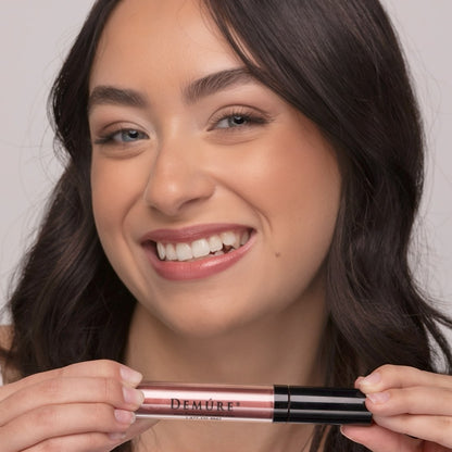 Woman wearing Demure Bronze Glow Lip gloss, holding a tube near her chin