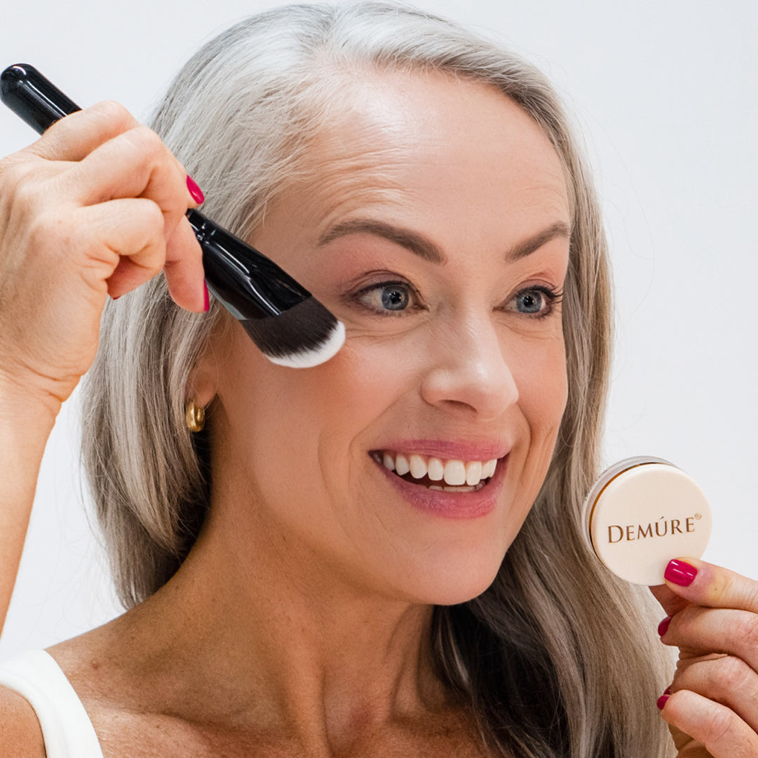 Woman applying Demure Peachy Blush with a contouring brush and jar 