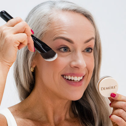 Woman applying Demure Peachy Blush with a contouring brush and jar 