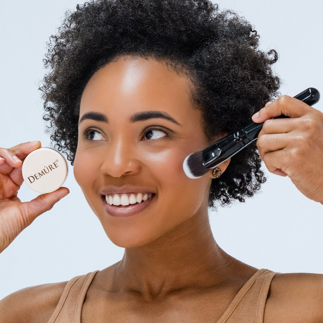Woman wearing Demure Pink Fusion mineral blush with a contour brush and holding a jar against a neutral 