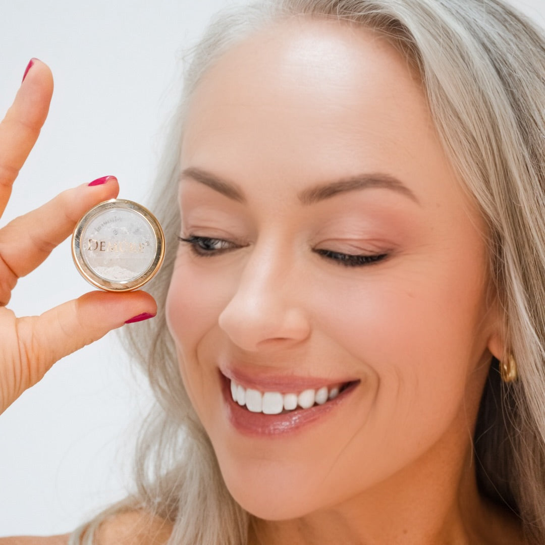 Woman wearing Demure eye colors Deep Champagne, Eggshell, & Pink Suede and holding a jar of eye color