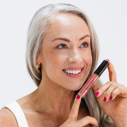 Woman holding a lip gloss tube wearing Dusty Rose Lip Gloss 74 and smiling against a light background