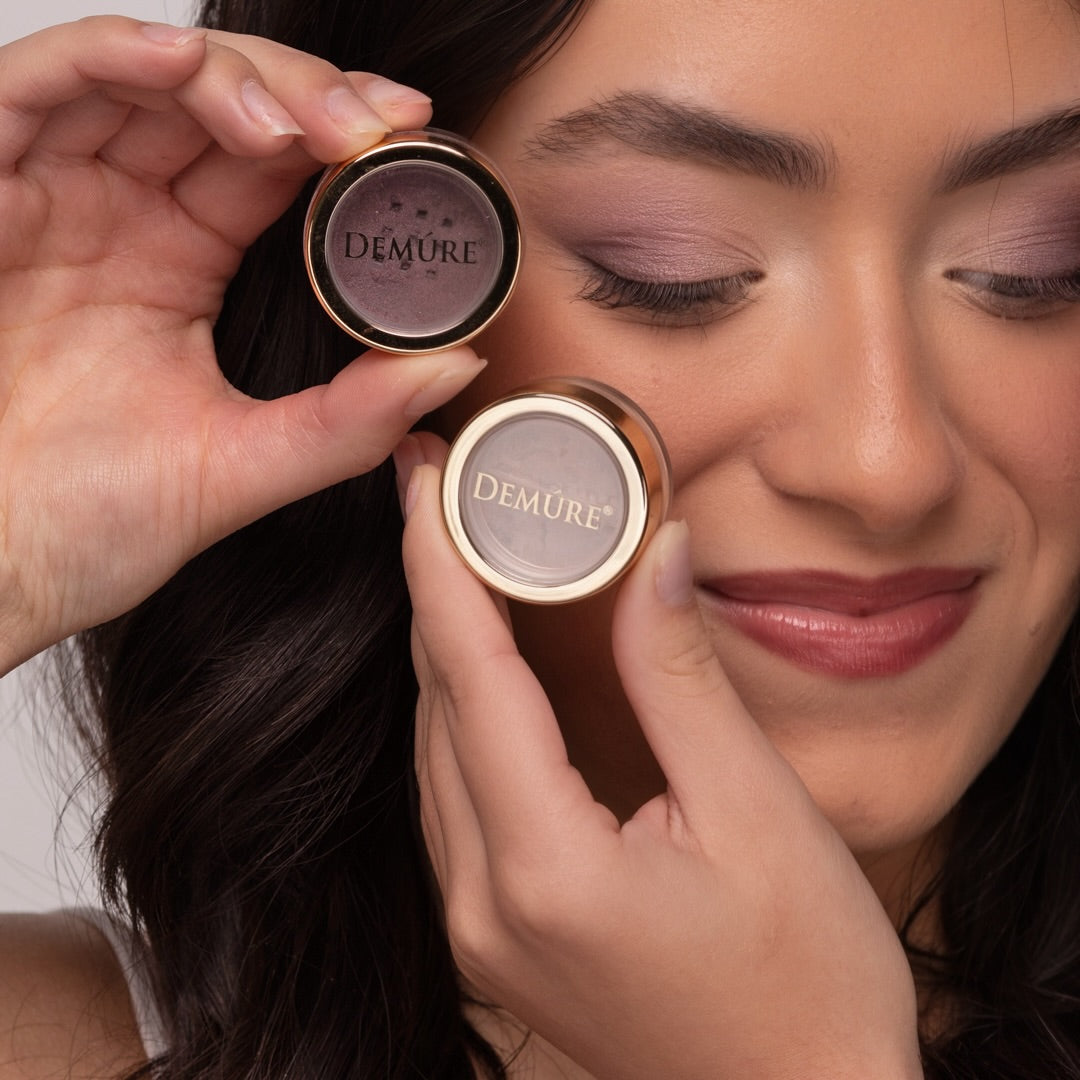Woman wearing Demure eye colors Spring Fever and Plum, holding eye color jars in her hands