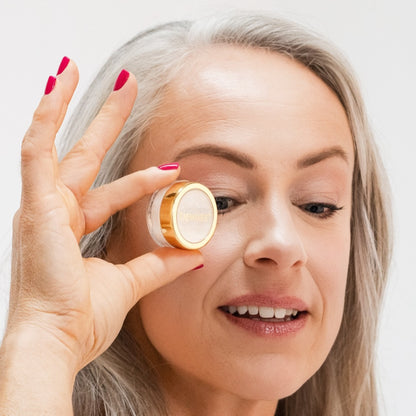 Woman wearing Demure Taupe eye color and holding a jar of the color near her eye.