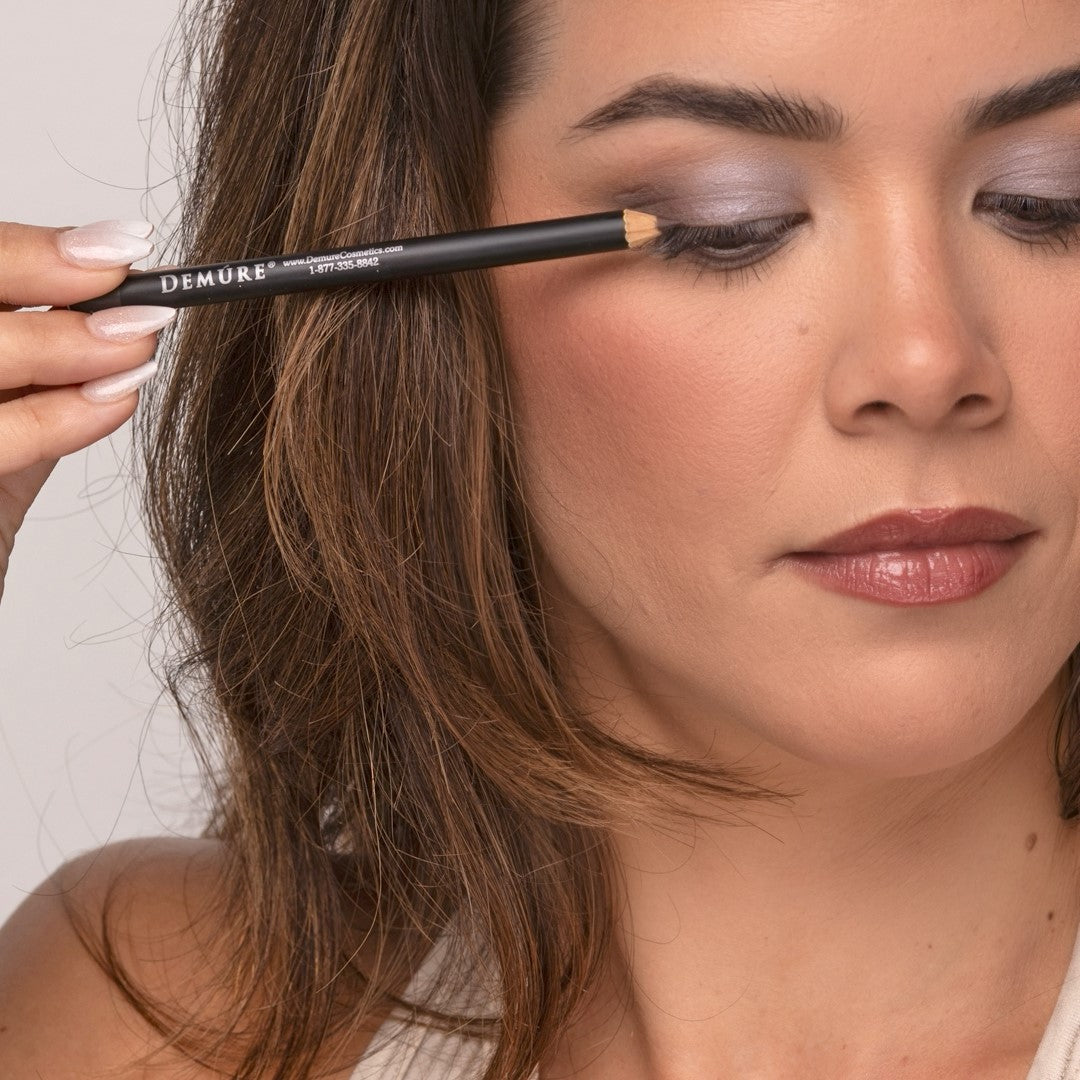 Close up of a woman applying Demure Dark Brown Eye Liner pencil looking down