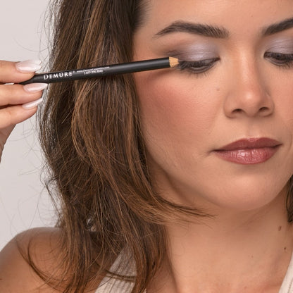 Close up of a woman applying Demure Dark Brown Eye Liner pencil looking down