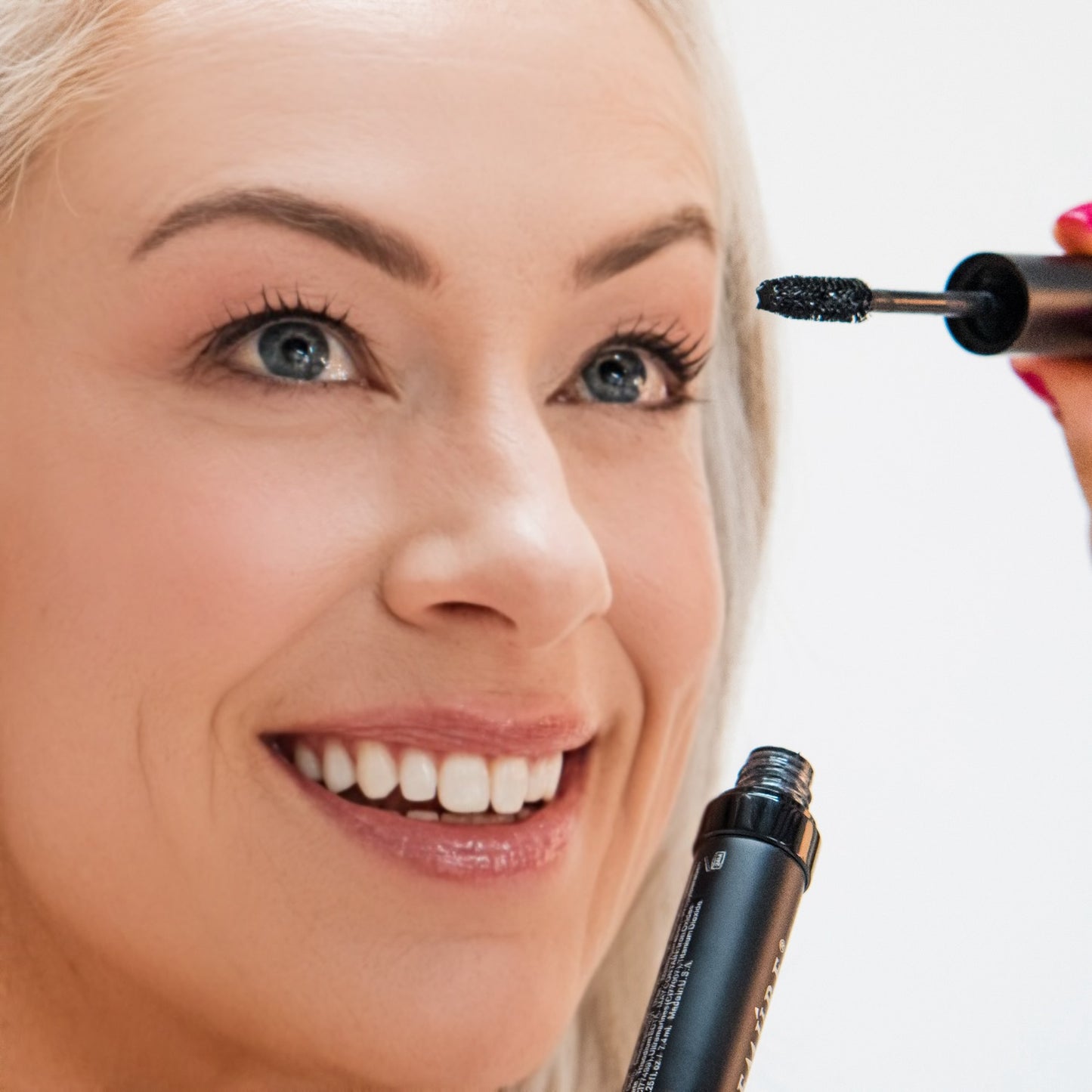 Woman applying Demure High Definition Black Mascara with a close-up of the product
