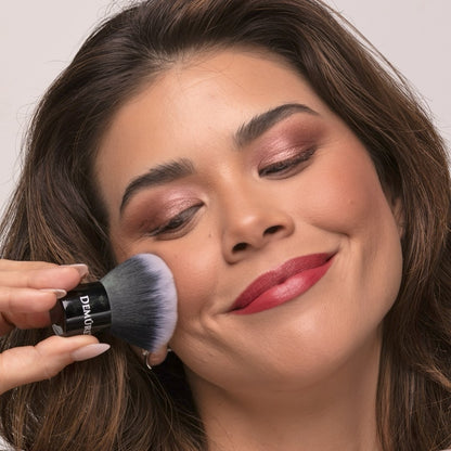 Woman using Kabuki Brush to apply makeup.