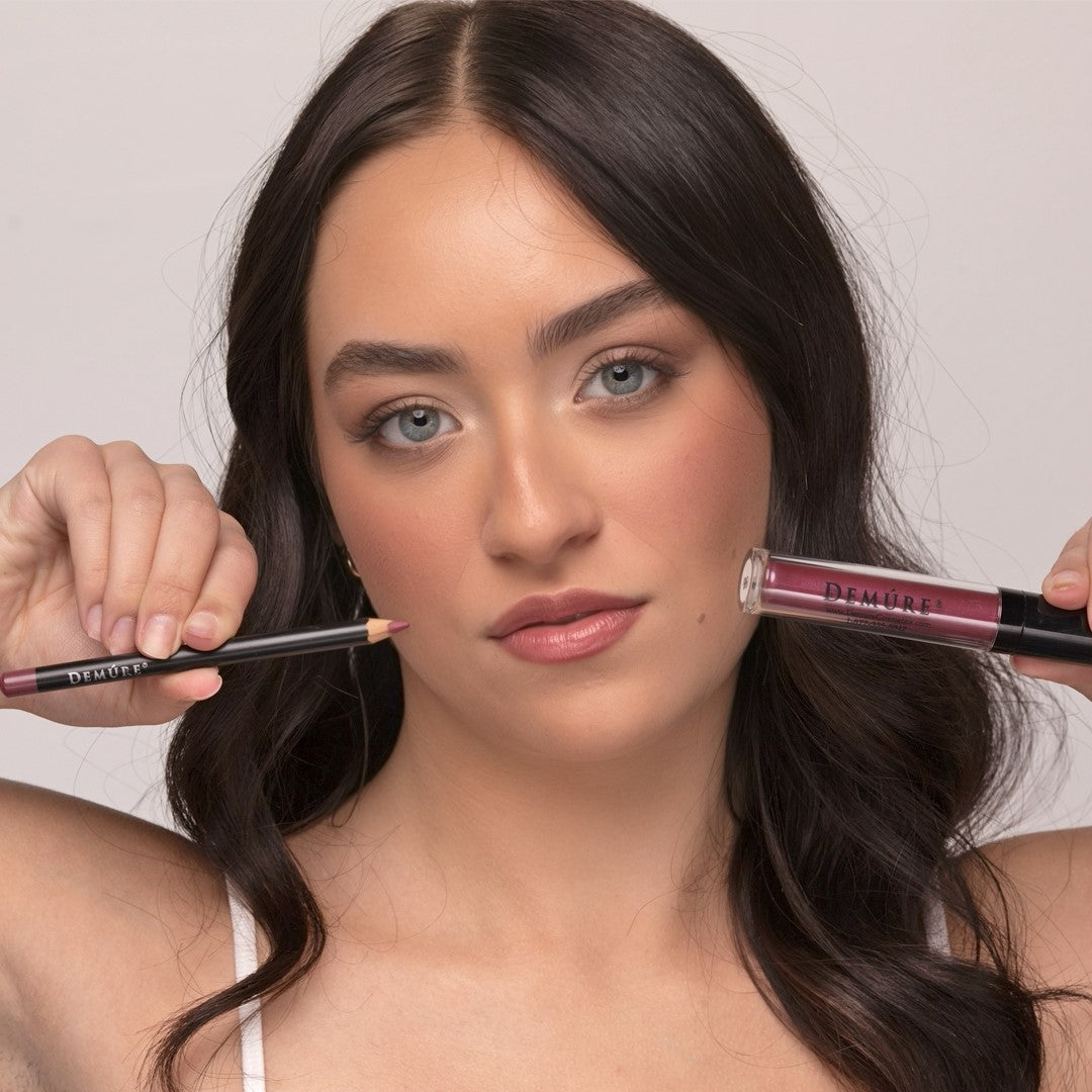 Woman wearing Demure Luscious Plum Lip Gloss and Antique Rose Lip Liner, and holding the lip gloss and liner in each hand.