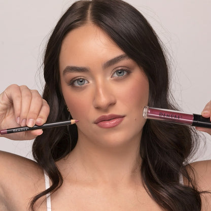 Woman wearing Demure Luscious Plum Lip Gloss and Antique Rose Lip Liner, and holding the lip gloss and liner in each hand.