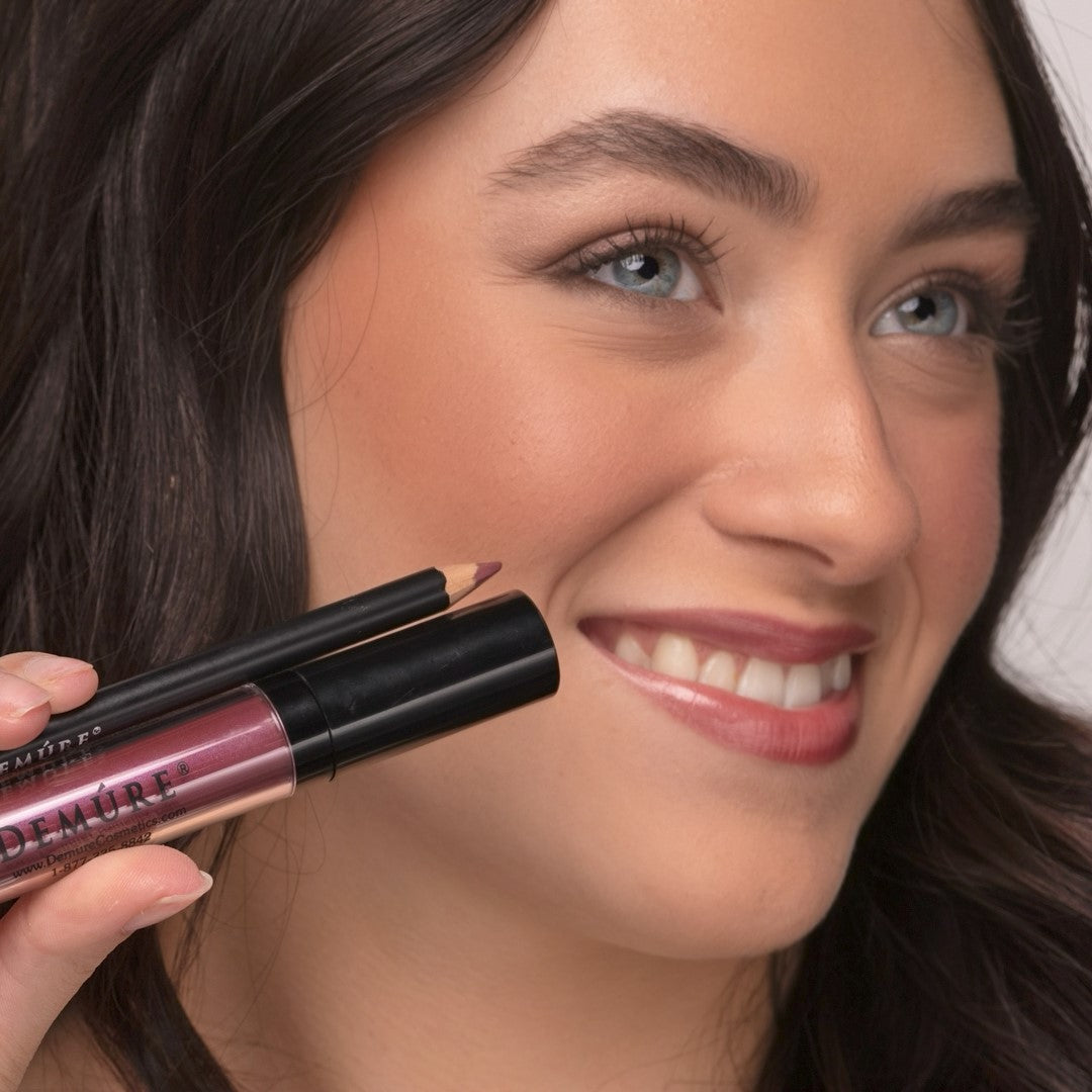 Woman wearing Demure Luscious Plum Lip gloss, and Antique Rose Lip Liner, holding  a tube and lip pencil. 