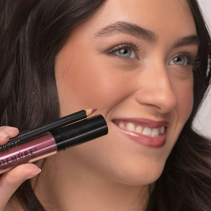 Woman wearing Demure Luscious Plum Lip gloss, and Antique Rose Lip Liner, holding  a tube and lip pencil. 