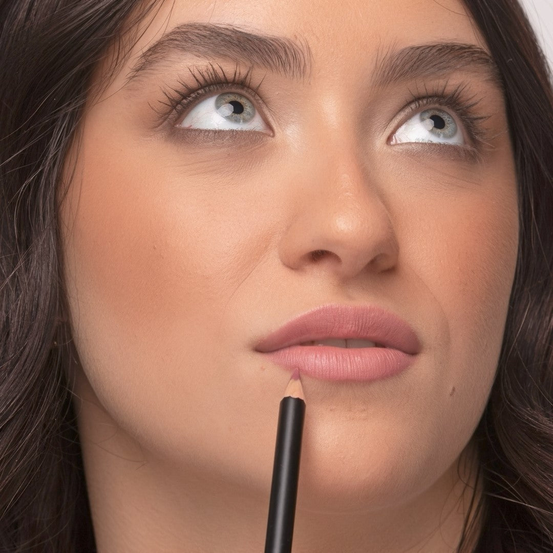Close up of a woman wearing Demure Antique Rose Lip Liner looking up, with the pencil near her bottom lip.