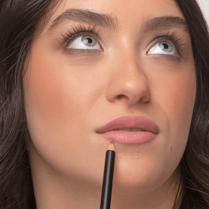 Close up of a woman wearing Demure Antique Rose Lip Liner looking up, with the pencil near her bottom lip.