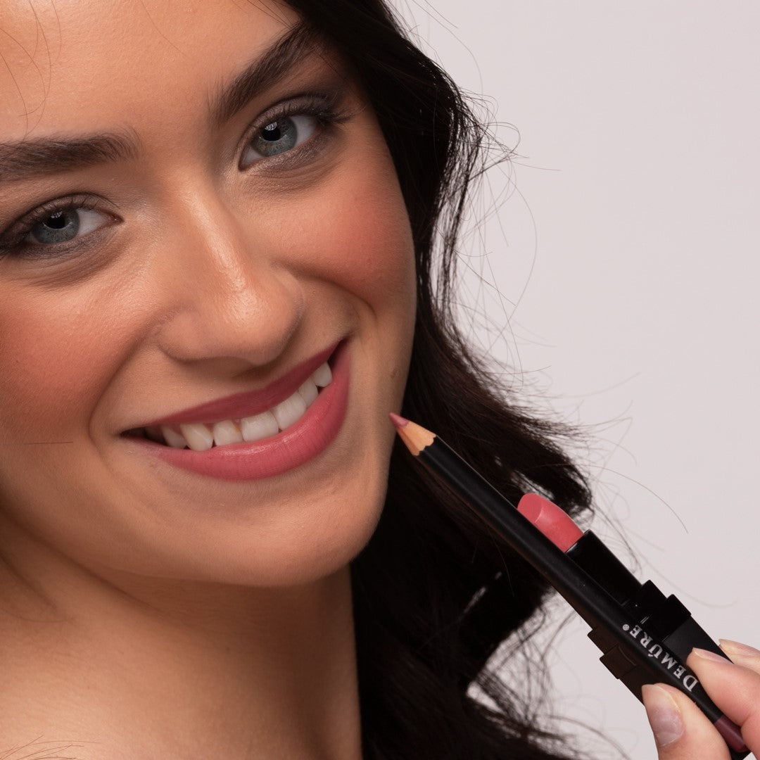 Close-up of a smiling woman wearing Demure Soft Rose Lipstick and Antique Rose Lip Liner, and holding both products in her hand.