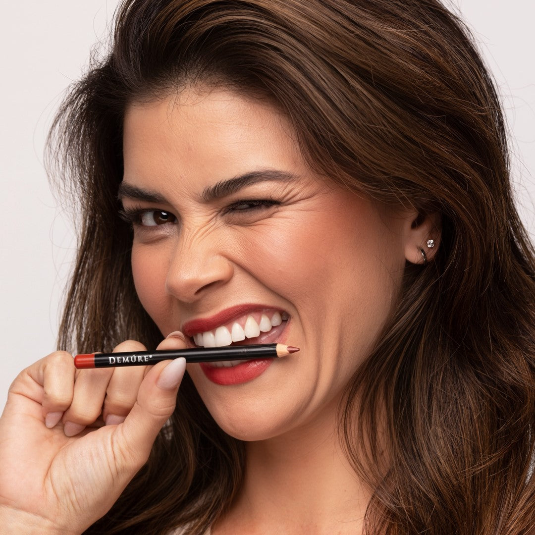 Sassy looking woman winking and holding a Demure Coffee Lip Liner in her teeth.