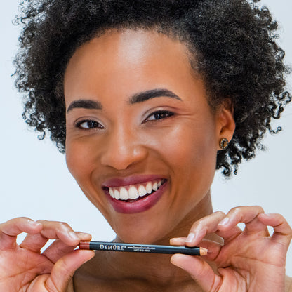 Smiling African American woman wearing Demure Lip Liner Sable Brown 46 and holding the pencil under her chin