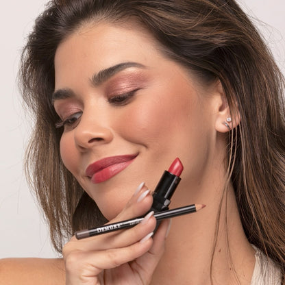 Woman wearing Demure Sweetheart Lipstick and Sable Brown Lip Liner, looking down, and holding the lipstick and lip pencil in her hands
