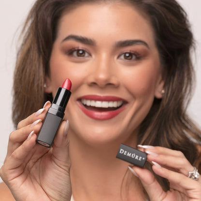 Woman wearing Demure Sweetheart Lipstick, holding an open lipstick in her hands.