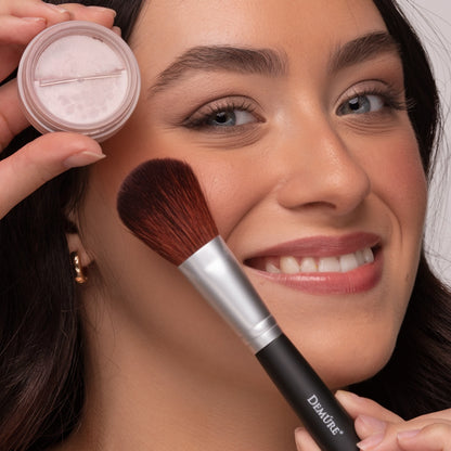Woman applying Demure Mauve Blush with a brush and holding a jar of makeup.