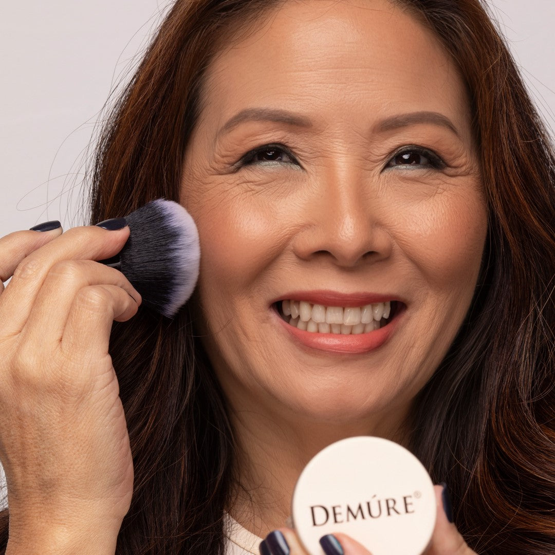 Asian woman applying Demure Medium Dark Foundation with a Kabuki brush.