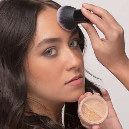 Woman using Kabuki Brush to apply foundation and holding a jar of makeup
