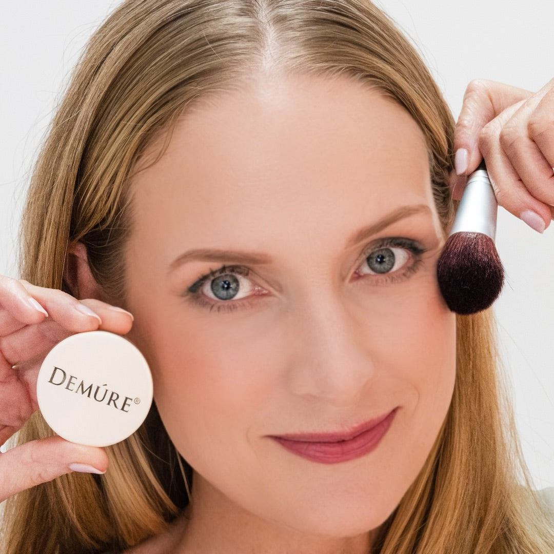 Woman wearing Mocha Rose Blush and holding a jar and a blush brush by her cheek