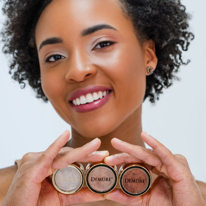 Woman wearing Demure Naked Glow Eye Color, Golden Coral Eye Color and Sienna Eye Color and holding the jars in her hands.