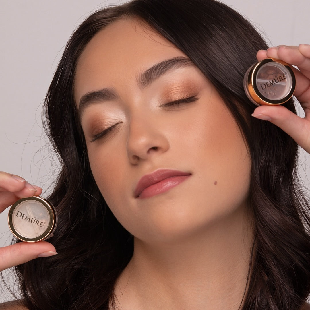 Woman with her eyes closed wearing Demure eye colors Naked Glow and Copper, holding eye color jars in her hands
