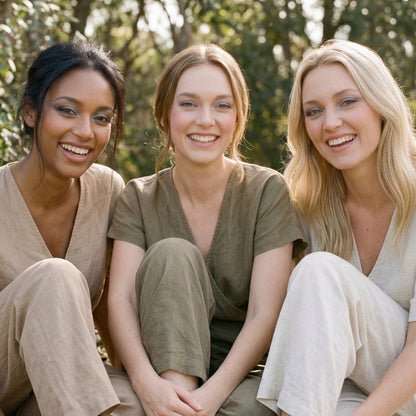 Three women sitting outdoors together, wearing Demure eye colors. Trees are blurred in the background.