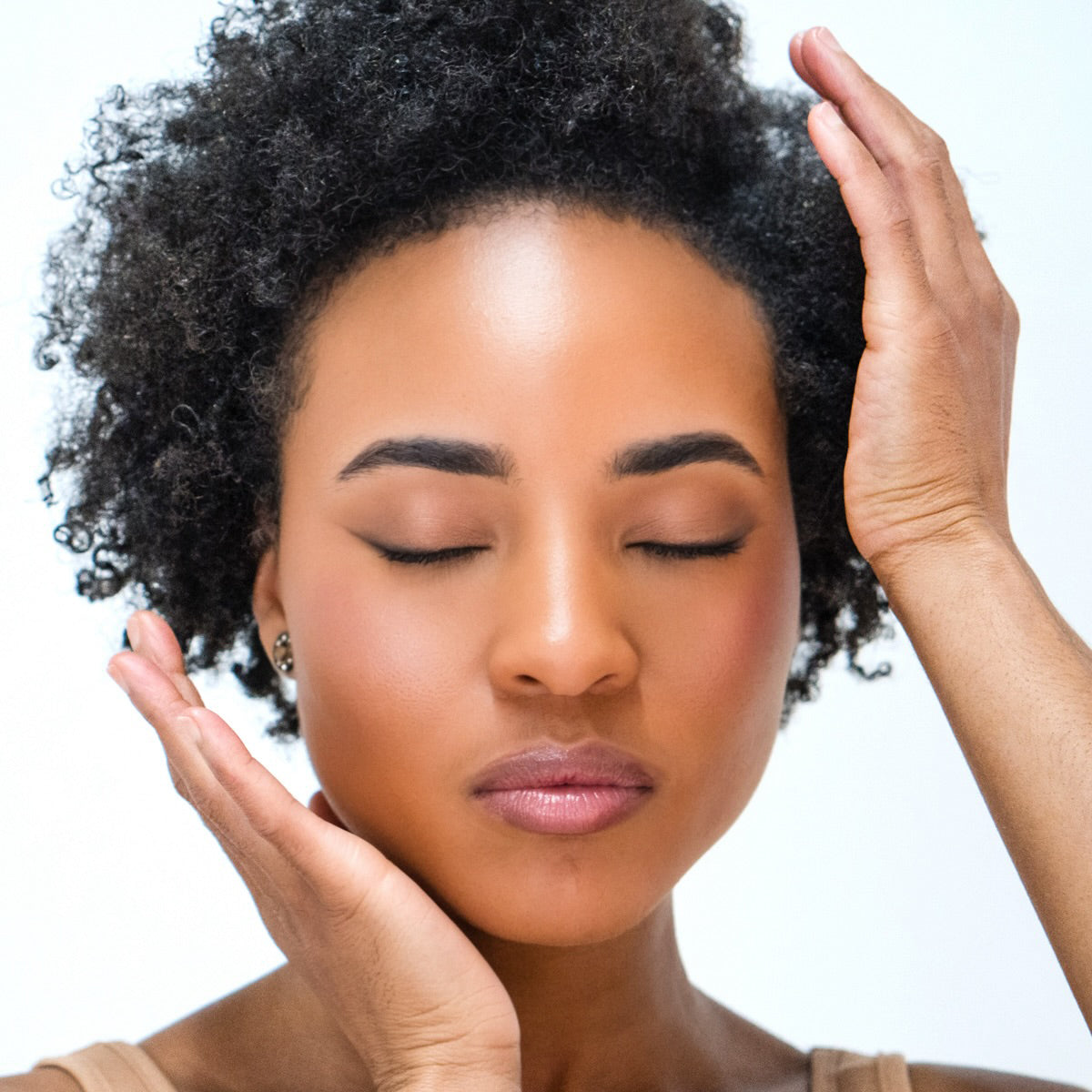 African American woman wearing Demure Original Concealer with natural hair touching her face against a light background