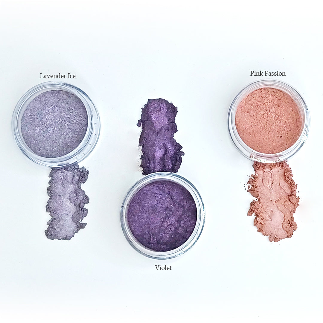 Open jars of Lavender Ice, Violet and Pink Passion shimmer eye colors with swatches of each color on white background
