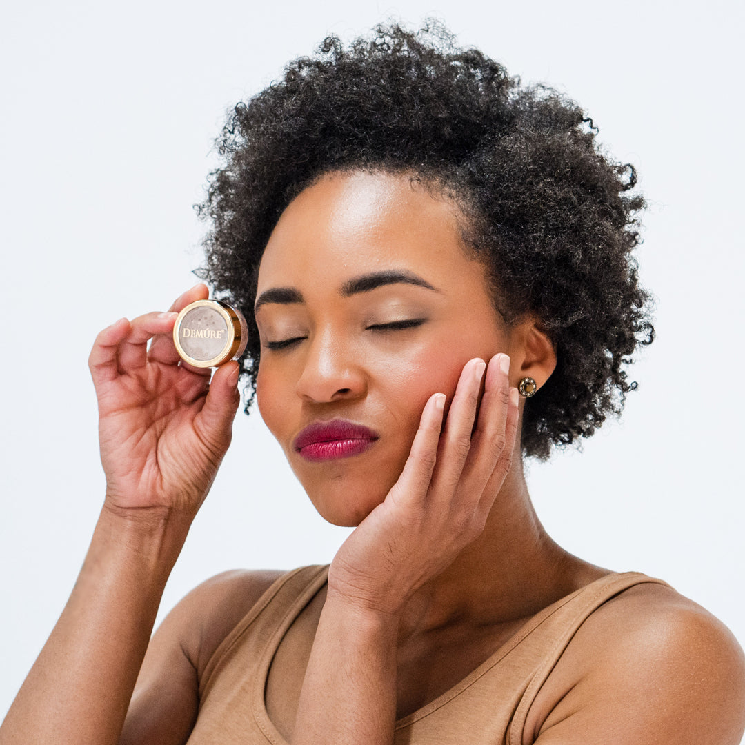 African American woman wearing Demure Taupe eye color with eyes closed holding the jar