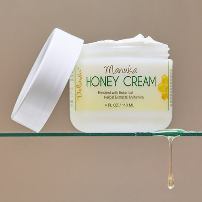 Jar of Deluvia Manuka Honey Cream with the lid off sitting on a glass shelf with honey dripping off the shelf