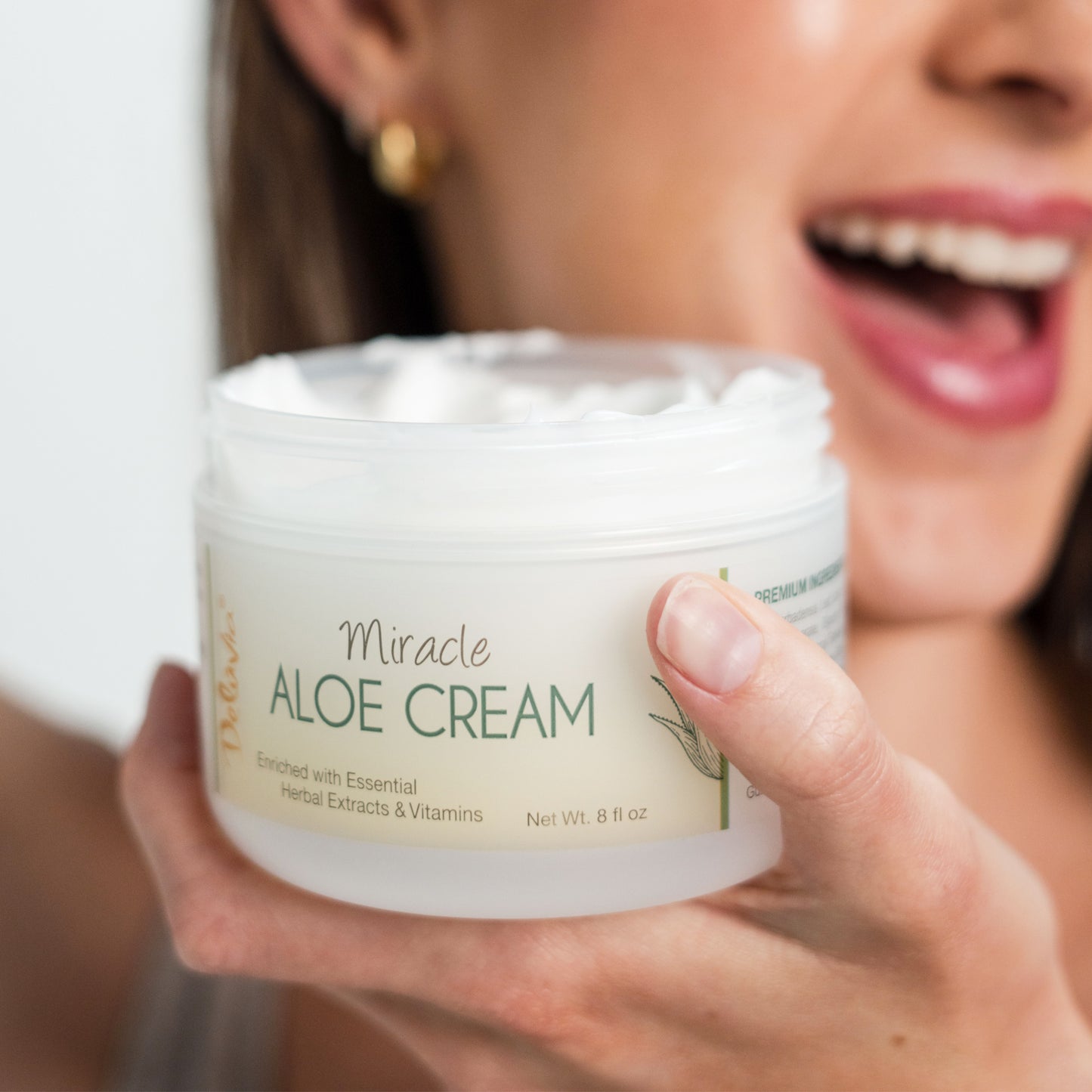 Smiling woman holding an open Deluvia Miracle Aloe Cream near her face