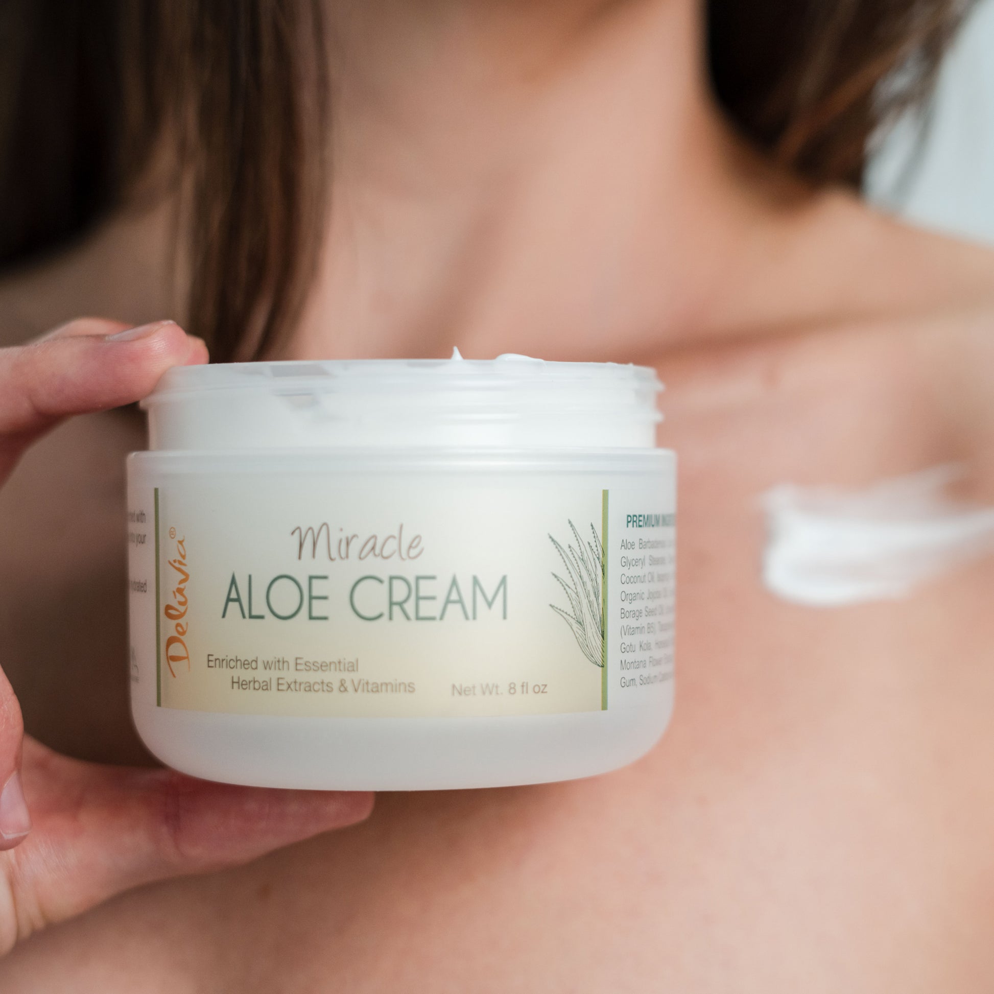 Woman holding an open Deluvia Miracle Aloe Cream with some cream on her neck